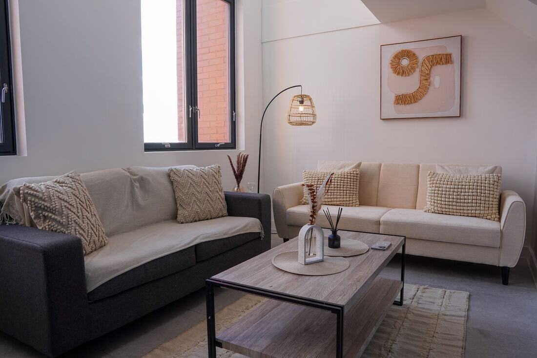 A styled living room with cream sofas, textured cushions and a rattan floor lamp.