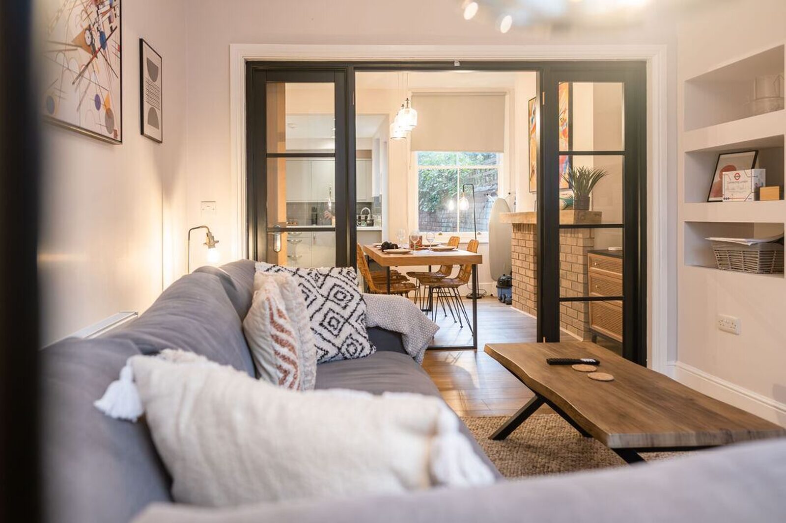 The living room of a managed short-let property, with Crittall doors opening through to a kitchen and dining table.